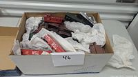 Box filled with various model train cars, including a visible red Texas Midland boxcar, and building parts wrapped in white tissue paper.
