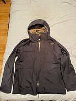 Photo of the black North Face windbreaker jacket laid flat, showing full front, hood, and sleeves.