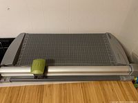 Overview of the full rotary paper trimmer with gray and silver frame and green rotary cutter handle on grid mat surface
