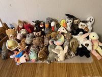Photo showing over 25 assorted Beanie Babies plush toys in various animal forms including a giraffe, owl, monkey, swan, duck, and bunny.