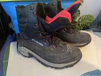 Side view of Columbia men's winter boots showing black exterior with red interior lining and rubber sole.
