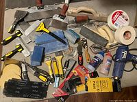 Lot of drywall tools including trowels, sanding sponges, sandpapers, heater, and tapes spread on floor