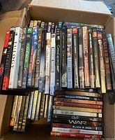 Photo showing a box filled with assorted DVDs, revealing multiple titles and various cover art designs.