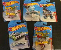 Five Hot Wheels vehicles in packages on flat surface.