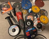 Complete lot of Milwaukee angle grinder with various grinding and cutting discs scattered around. Side handle and wrench included with grinder.