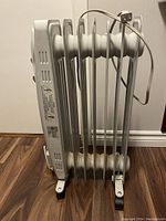 Front and side view of the oil-filled heater showing its fins, caster wheels, and power cord.