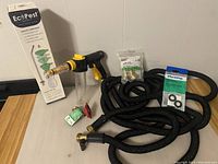 Expandable black garden hose coiled with Eco Pest sprayer nozzle attached and assorted connectors on table