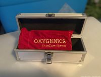 Closed metal case with red velvet storage bag inside, showing Oxygenics embroidered branding