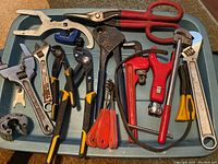 Full view of all plumber's tools arranged on a flat surface showing various pipe wrenches, pliers, cutters, and specialized wrenches.