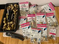 Loose brass pipe fittings in black bin and various SharkBite PEX fittings in unopened packaging laid out on table