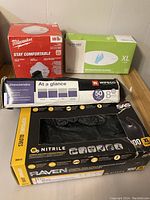 Photo showing four boxes: Milwaukee N95 masks (red box), green box with Pri-Med nitrile gloves, Wipeco black nitrile gloves box with 50 gloves, and large black and yellow Raven nitrile gloves box with 100 gloves size XL