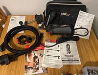 Overall lot showing Rotozip RZ1500 spiral saw, flexible hose, guide attachments, storage bag, and multiple manuals spread out on a surface.