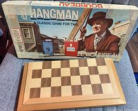 Original packaging of the Milton Bradley Hangman game with foldable wooden chess board underneath