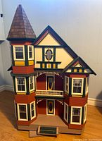 Front exterior view showing three-story structure, turret, painted red with green and yellow trim and wood shingle roof