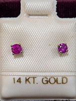 Pair of 14K white gold ruby stud earrings displayed on white padded card with gold 14 KT. GOLD lettering.