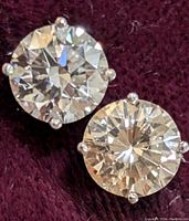 Front view of both round brilliant-cut diamonds in four-prong settings on a burgundy background