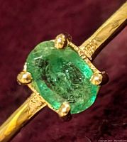 Close-up of oval natural emerald gemstone set in 10K yellow gold ring, detailing the emerald's color and inclusions along with gold prongs and textured band elements.