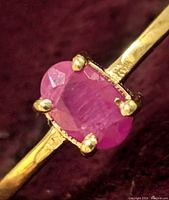 Close-up front view of the oval ruby set in four-prong 10K gold ring showing the gemstone's faceting and color.