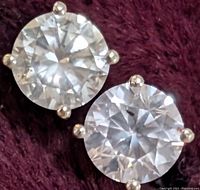 Two round brilliant cut diamonds in four-prong settings on burgundy background