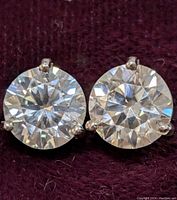 Close-up front view of two round moissanite stones in four-prong white gold settings on burgundy fabric.