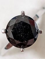 Top-down view of round black diamond and prong setting.
