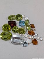 Photo showing a spread of assorted genuine faceted gemstones in various colors and shapes on a white surface.