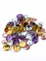 Close-up photo of mixed assorted genuine faceted gemstones in a pile showing multiple colors including purple, yellow, pink, blue, and green.
