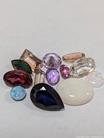 Overhead photo of a collection of various faceted and cabochon gemstones of multiple colors and shapes on a white background.