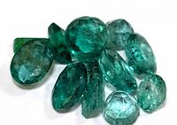 Close-up view of the pile of green emerald gemstones showing their natural inclusions and various cuts.