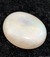 Close-up image of the oval-shaped genuine opal gemstone with visible play-of-color on a black fabric background.