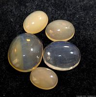 Five oval cabochon genuine opal stones with different sizes and milky/translucent hues on a black cloth background.