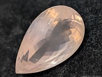 Close-up of pear-shaped faceted rose quartz gemstone on black background showing clarity and faceting details.