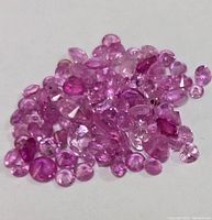 Pile of loose pink to deep pink/red faceted ruby gemstones on a white background.