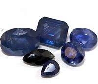 Group of six genuine sapphire gemstones in various cuts and shades of blue and black.