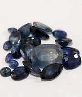 Close-up photo of multiple loose genuine sapphire gemstones in different sizes and cuts on white background