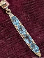 Close-up of elongated sterling silver pendant with four oval blue topaz gemstones set vertically.