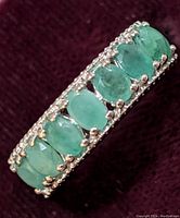 Close-up photo of sterling silver ring with oval emerald gemstones all in a row on a dark red background.