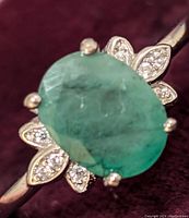 Close-up front view of oval emerald with diamond accent petals on sterling silver band