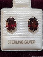Front view of two oval garnet earrings set in sterling silver prong mountings on white background showing markings.