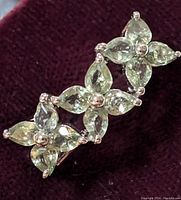 Close-up photo of the sterling silver ring with green sapphire stones arranged in floral clusters against a dark background.