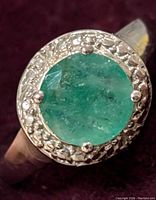 Close-up photo of a sterling silver ring with a round natural emerald stone, showing textured bezel setting.