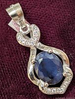 Front view of sterling silver pendant with natural oval sapphire and cubic zirconia stones on heart and loop.