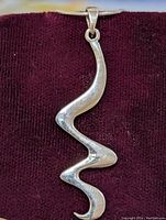 Close-up front view of the abstract-shaped silver pendant against a dark fabric background.