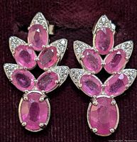 Close-up front view of the pair of ruby and clear stone sterling silver earrings on dark fabric background.