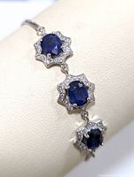 Close-up photo showing the sterling silver bracelet with three oval sapphire stones surrounded by cubic zirconia in a star-shaped halo setting.