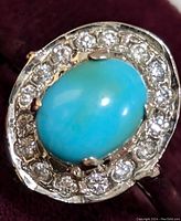 Close-up front view of ring showing oval turquoise centerpiece and clear CZ stones arranged around it on sterling silver band.