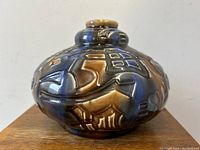 Front angle of the Art Deco pottery vase showing embossed abstract geometric and animal designs with blue and brown glaze.