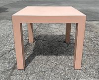 Full frontal photo of the pink laminate square side table outdoors on pavement showing its shape and overall condition.