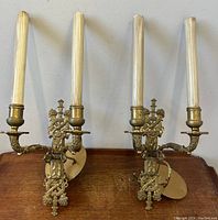 Pair of antique brass twin-light wall sconces with ornate Empire Napoleonic style detailing and faux candle lights
