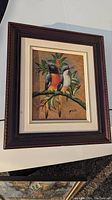 Full view of the framed oil painting showing two exotic birds on a leafy branch, painted over real dried leaves.